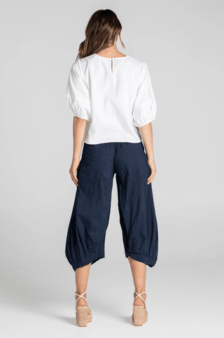 Woman wearing a white puff sleeve blouse and navy blue cropped wide-leg culotte pants.
