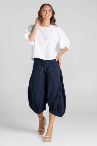 Woman wearing a white puff sleeve blouse and navy blue wide-leg harem pants.