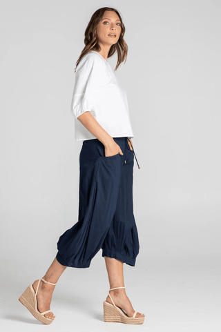 Woman wearing white puff sleeve top and navy blue cropped harem pants with wedge sandals.