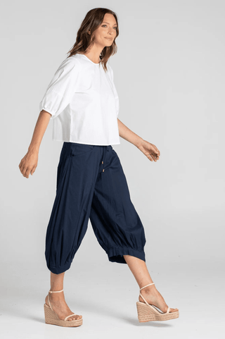 Woman wearing white puff sleeve blouse and navy blue cropped harem pants with wedge sandals.