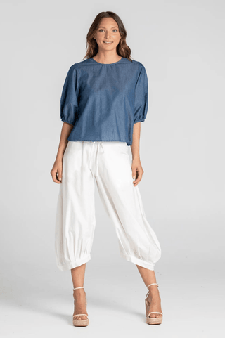 Woman wearing a blue short-sleeve puff sleeve top and white wide-leg cropped trousers.