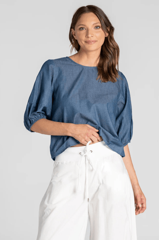 Woman wearing a blue denim puff sleeve blouse and white linen drawstring pants.