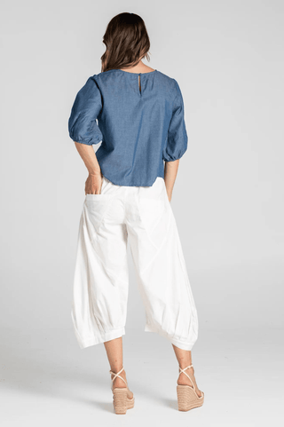 Woman in a blue puff sleeve denim blouse and white wide-leg cropped trousers.