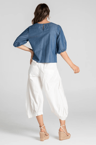 Woman wearing a blue denim puff sleeve top and white wide-leg cropped trousers with wedge sandals.