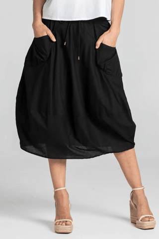 Woman wearing black midi skirt with pockets and white wedge sandals.