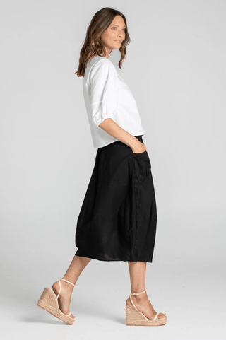 Woman wearing a white puff sleeve blouse and black midi skirt with wedge espadrille sandals.