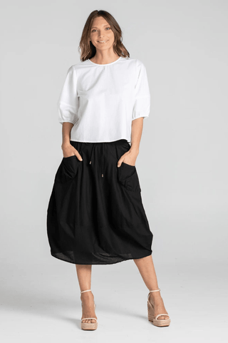 Woman wearing a white puff sleeve blouse and black midi skirt with pockets.