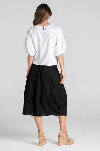 Woman wearing a white puff sleeve blouse and black midi skirt with wedge sandals.