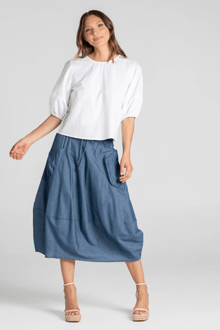 Woman wearing a white puff sleeve blouse and a blue denim midi skirt with pockets.