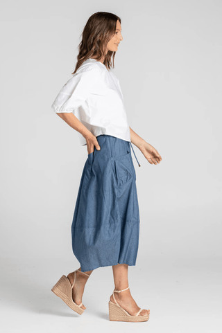 Woman wearing a white puff sleeve blouse and blue denim midi skirt with wedge sandals.