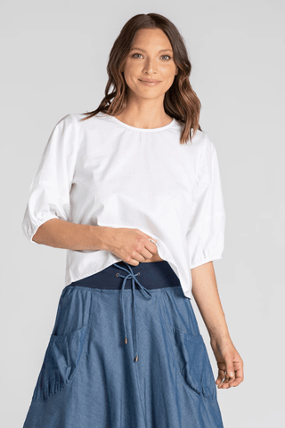 Woman wearing a white puff sleeve blouse and blue denim maxi skirt with drawstring waist.