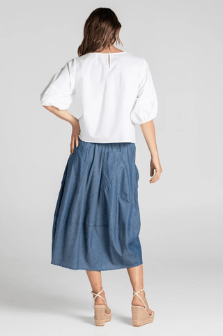 Woman wearing a white puff sleeve blouse and a blue midi skirt with wedge sandals.