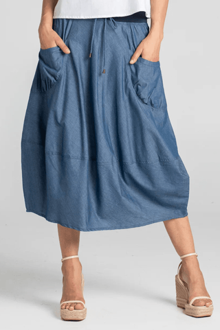 Woman wearing a blue denim midi skirt with large front pockets and a drawstring waist.