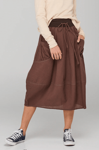 Woman wearing a brown linen midi skirt with drawstring waist and large pockets.