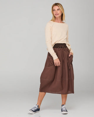 Woman wearing a cream long-sleeve top and brown midi skirt with pockets and drawstring waist.