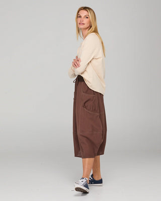 Woman wearing a cream long sleeve top and brown wide-leg culotte pants with sneakers.