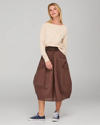 Woman wearing a cream long sleeve top and brown midi skirt with drawstring waist.