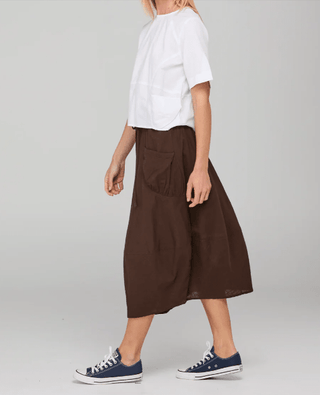 Woman wearing a white t-shirt, brown midi skirt, and blue canvas sneakers.