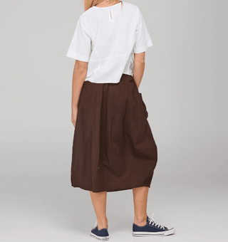 Rear view of a woman wearing a white t-shirt and a brown midi skirt with navy sneakers