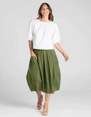 Woman wearing a white puff-sleeve top and an olive green midi skirt with pockets.