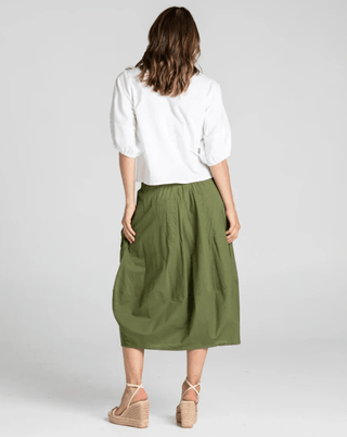 Rear view of a woman wearing a white blouse and an olive green midi skirt with wedge sandals.