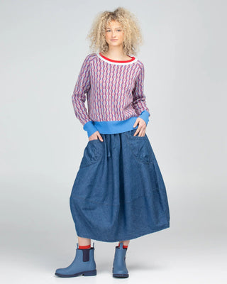 Woman wearing a patterned red and white sweatshirt and a long blue denim skirt with boots.