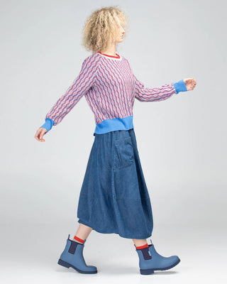 Woman wearing a patterned knit sweater, blue denim midi skirt, and blue rain boots.