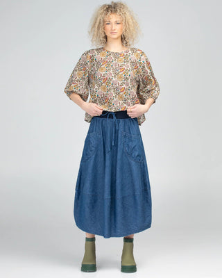 Woman wearing a floral printed blouse and a long blue denim skirt with olive boots.