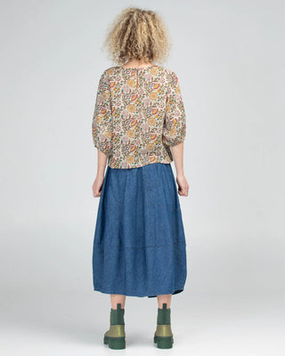Back view of a woman wearing a floral print blouse, blue denim midi skirt, and green boots.
