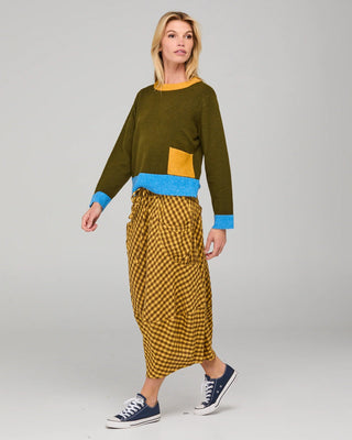 Woman wearing an olive green colorblock sweatshirt and mustard gingham midi skirt.