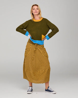 Woman wearing an olive green sweatshirt with blue trim and a mustard checkered maxi skirt.