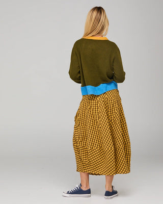 Woman wearing an olive green sweater with blue trim and a mustard yellow gingham midi skirt.