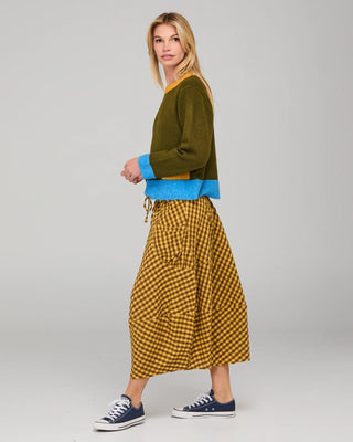 Woman wearing an olive green sweatshirt with blue trim and a mustard yellow gingham skirt.