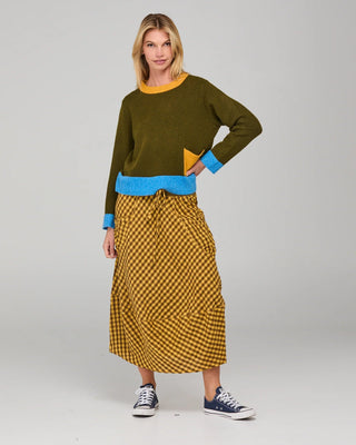 Woman wearing an olive green sweatshirt with blue trim and a yellow checkered midi skirt.