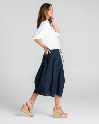 Woman wearing a white puff sleeve blouse and navy blue midi skirt with wedge sandals.