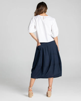 Woman wearing a white puff sleeve blouse and navy blue midi skirt with platform sandals.