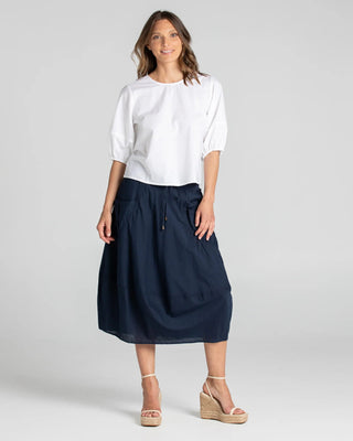 Woman wearing a white puff sleeve blouse and navy blue midi skirt with wedge sandals.