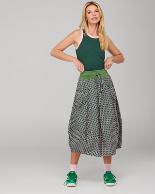 Woman wearing a green tank top and a patterned midi skirt with green sneakers.