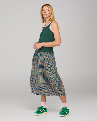 Woman wearing a green tank top, printed midi skirt, and green sneakers.