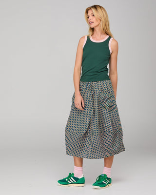 Woman wearing a dark green tank top, patterned midi skirt, and green sneakers.