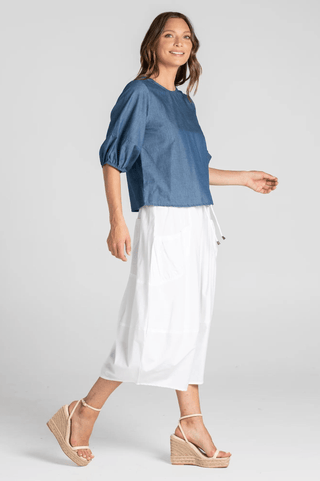 Woman wearing a blue denim puff sleeve top and white midi skirt with wedge sandals.