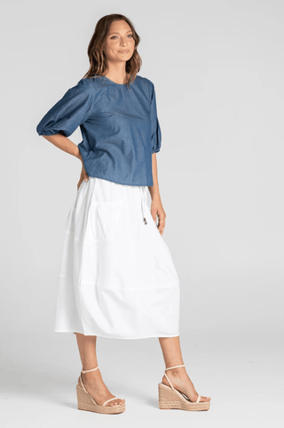 Woman wearing a blue puff sleeve top and white midi skirt with wedge sandals.