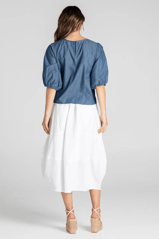 Woman wearing a blue puff sleeve denim top and white midi skirt with wedge sandals.