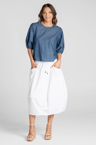 Woman wearing a blue puff sleeve top and white midi skirt with pockets.