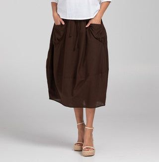 Woman wearing a dark brown midi skirt with large pockets and white sandals.