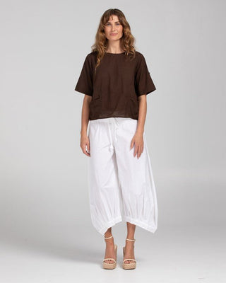 Woman wearing a brown short-sleeve top and white wide-leg palazzo pants with wedge sandals.