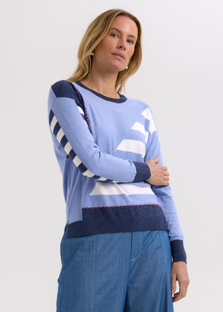 Woman wearing a blue and white geometric pattern knit sweater and blue denim pants.