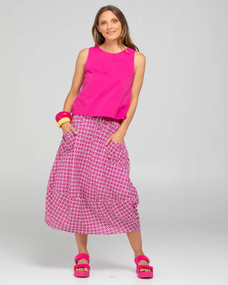 Woman wearing a bright pink sleeveless top and patterned pink maxi skirt with platform sandals.