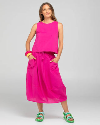 Woman wearing a bright pink sleeveless top and matching maxi skirt with green sandals.