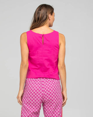 Woman wearing a bright pink sleeveless linen top and patterned pink and white trousers.
